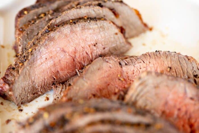 Broiled steak on a white platter, sliced into thin pieces.