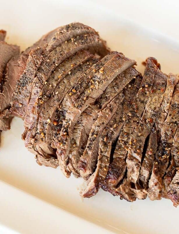 Broiled steak on a white platter, sliced into thin pieces.
