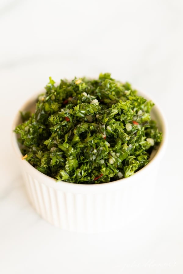A small white bowl of chimichurri on a marble countertop