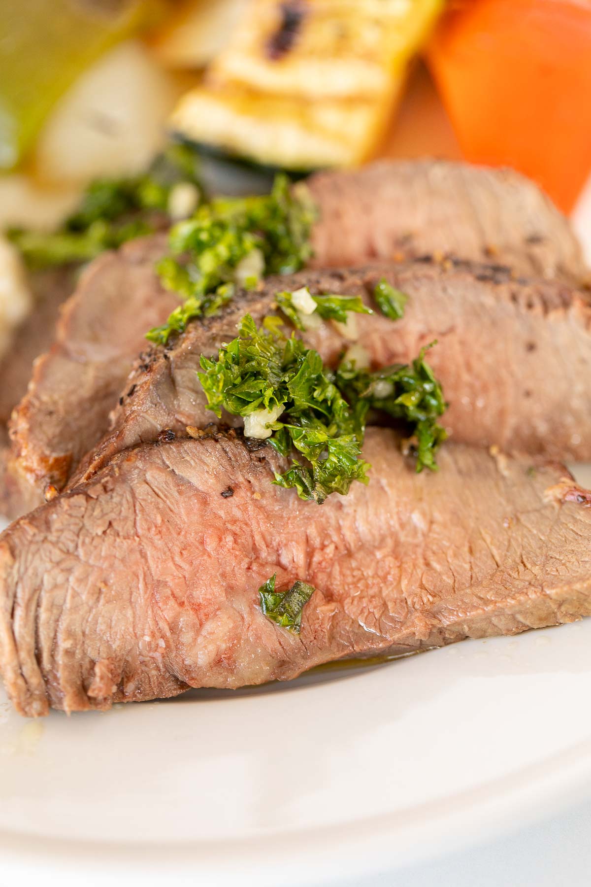 Sliced steak on a white plate, topped with chimichurri.