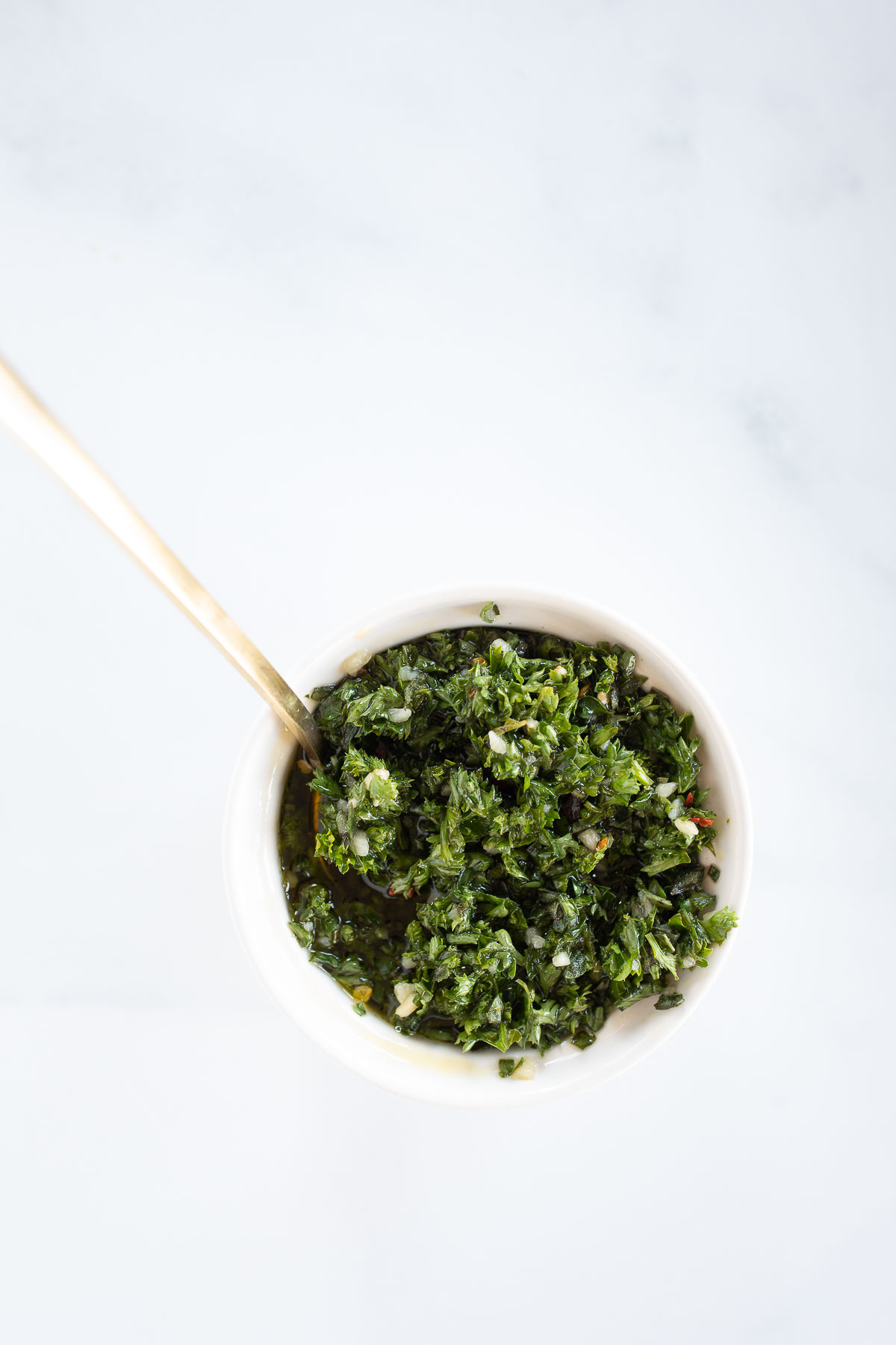 A white bowl of chimichurri on a marble countertop.