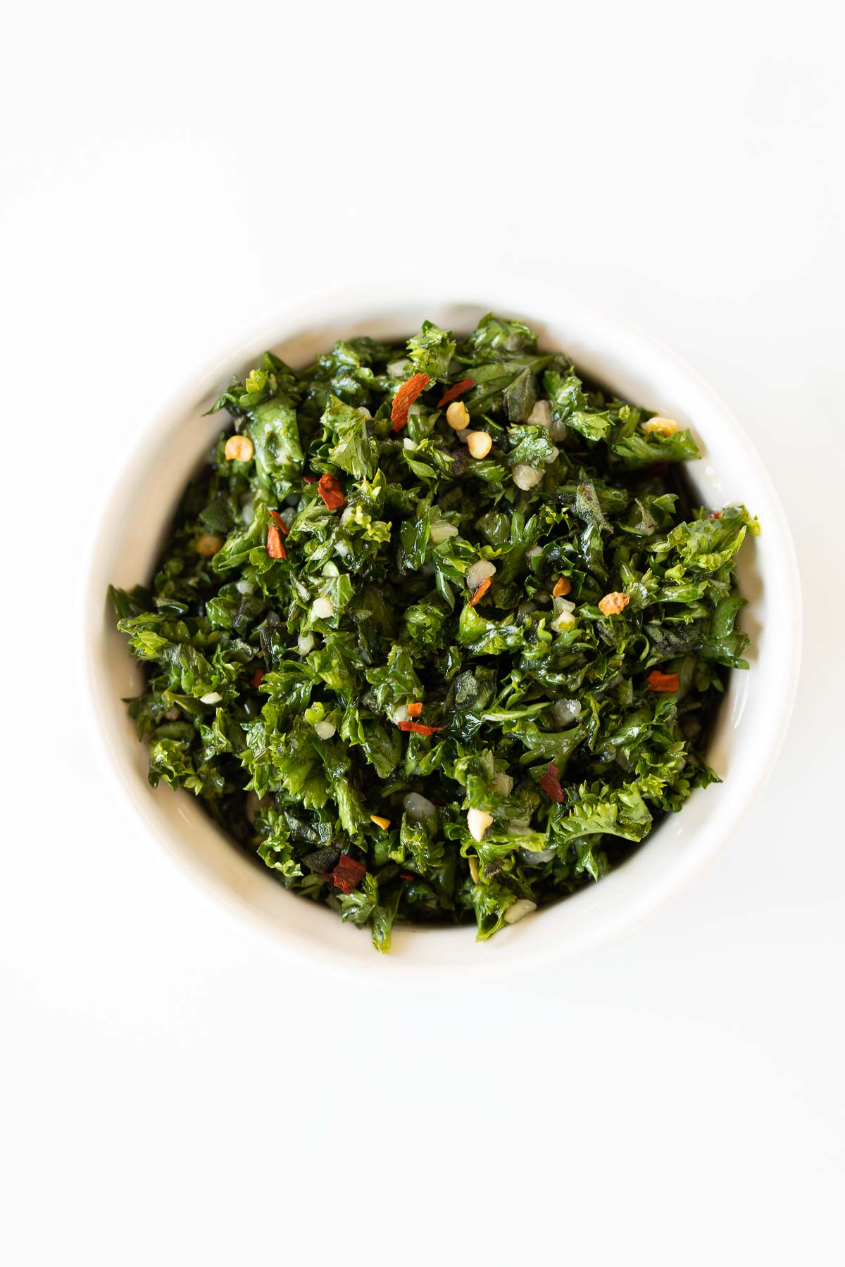 A white bowl of chimichurri on a marble countertop.