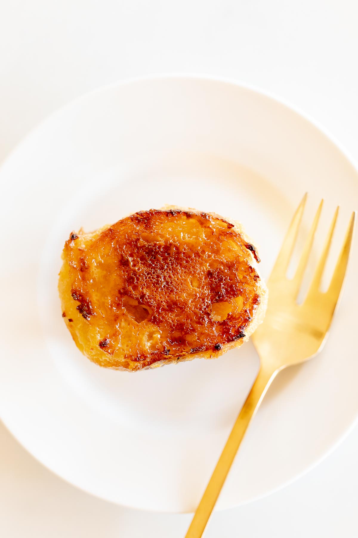 A slice of creme brulee french toast on a white plate with a gold fork.