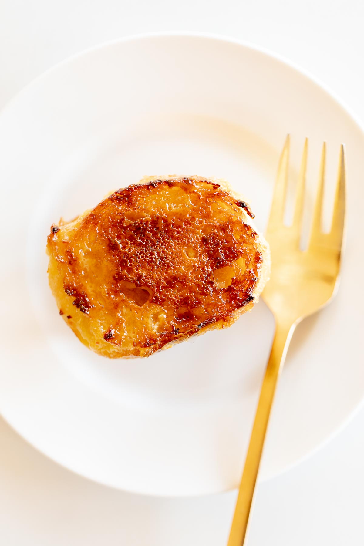 A slice of creme brulee french toast on a white plate with a gold fork.