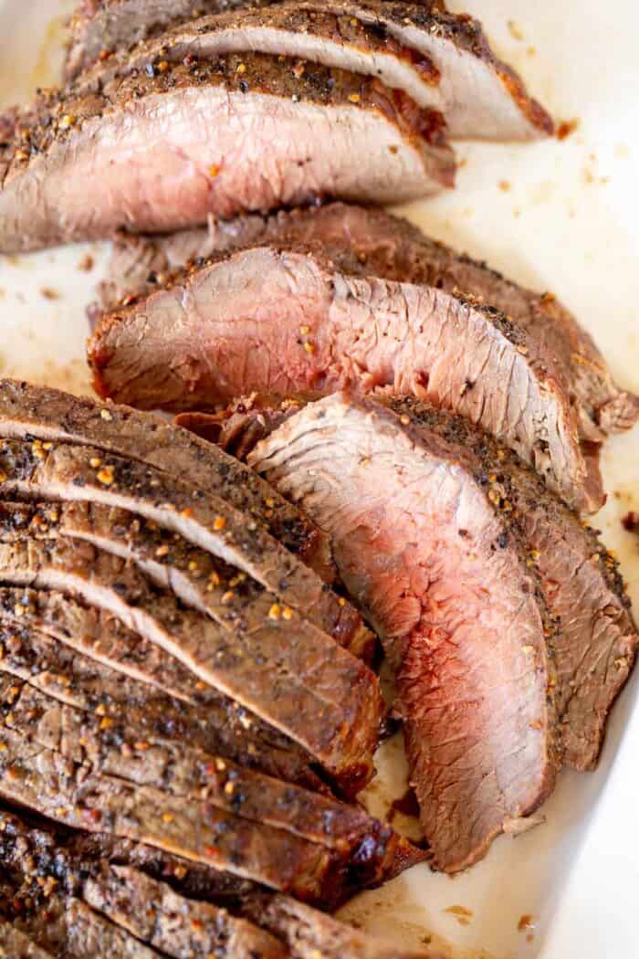 Broiled steak on a white platter, sliced into thin pieces.