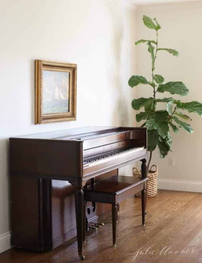 piano with painting above and fiddle leaf fig to side