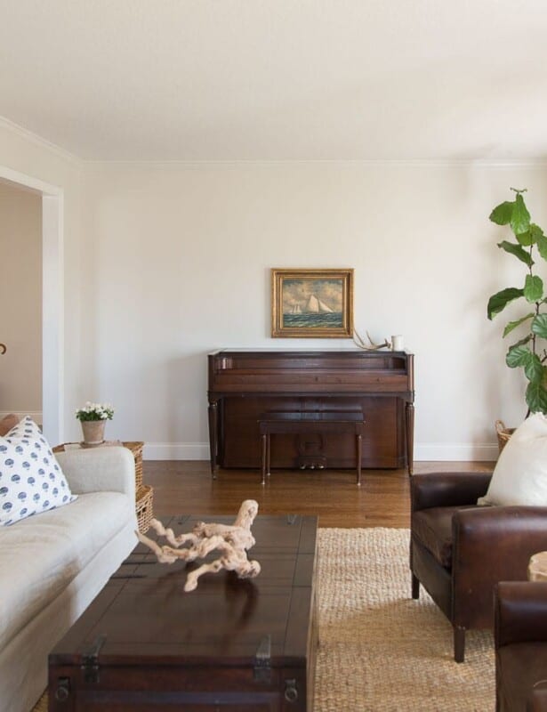 A cream colored family room with dark furniture and a vintage piano and large fiddle leaf fig against one wall.