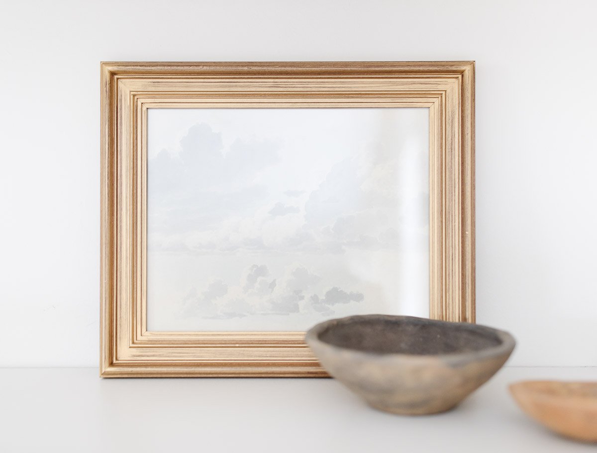 A framed print of clouds and a bowl on a table sourced from Studio McGee's public domain art collection.