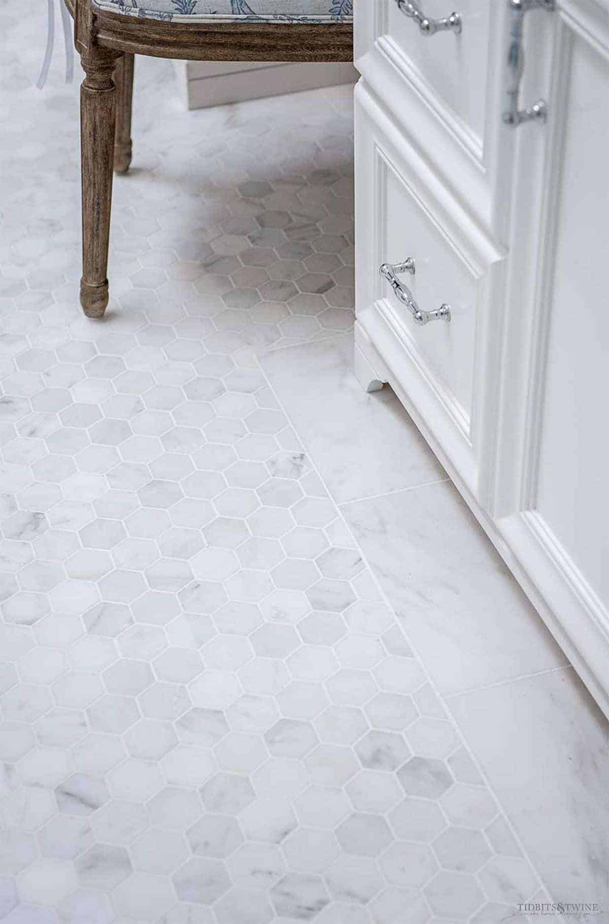 Small hexagon tile on the floor of a bathroom, white vanity base to the right.