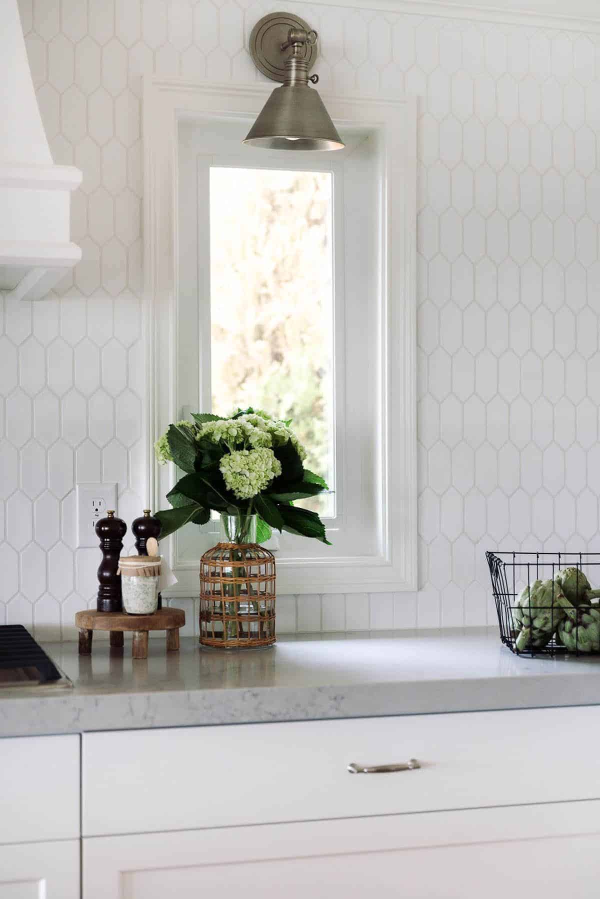 A kitchen with white hexagon tile backsplash and white cabinets.