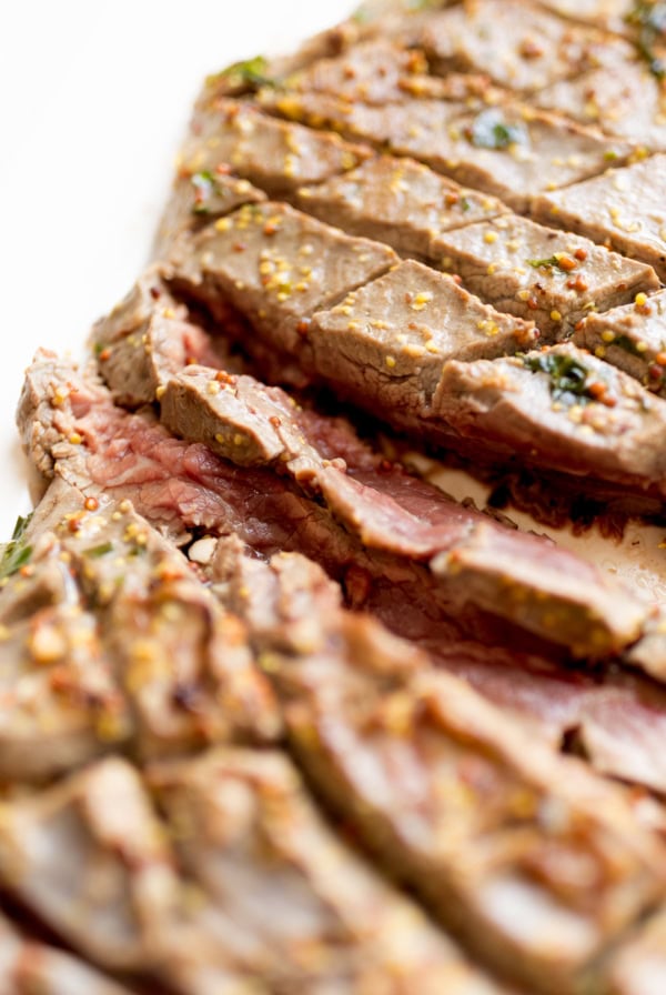 Close-up of sliced, seasoned broiled steak cooked to a medium-rare doneness, showing a pink interior and brown exterior with visible herbs and spices.