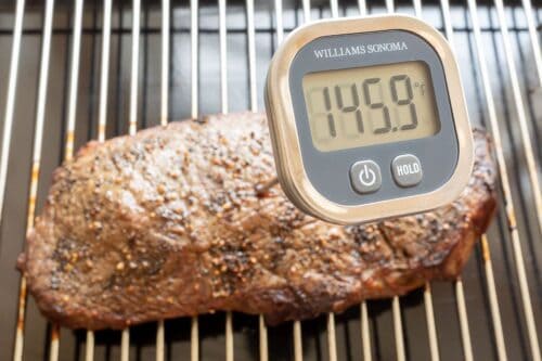 A piece of broiled steak on a broiling pan with a digital thermometer showing 145.9 degrees in a tutorial for how to broil steak.