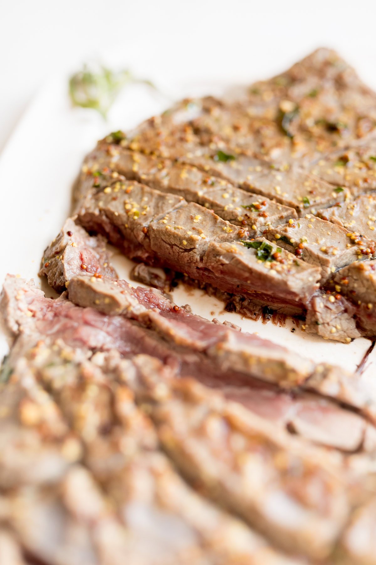 Close-up of sliced, medium-rare broiled steak on a white surface, seasoned with herbs and spices.