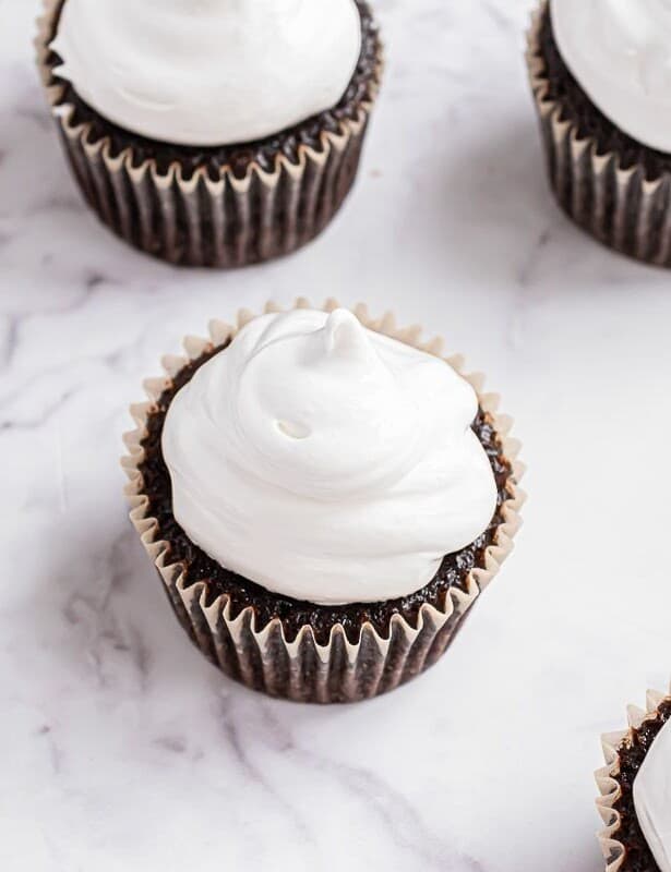 Chocolate cupcakes on a white marble surface, topped with marshmallow icing.