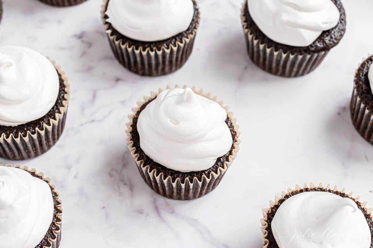 Chocolate cupcakes on a white marble surface, topped with marshmallow icing.
