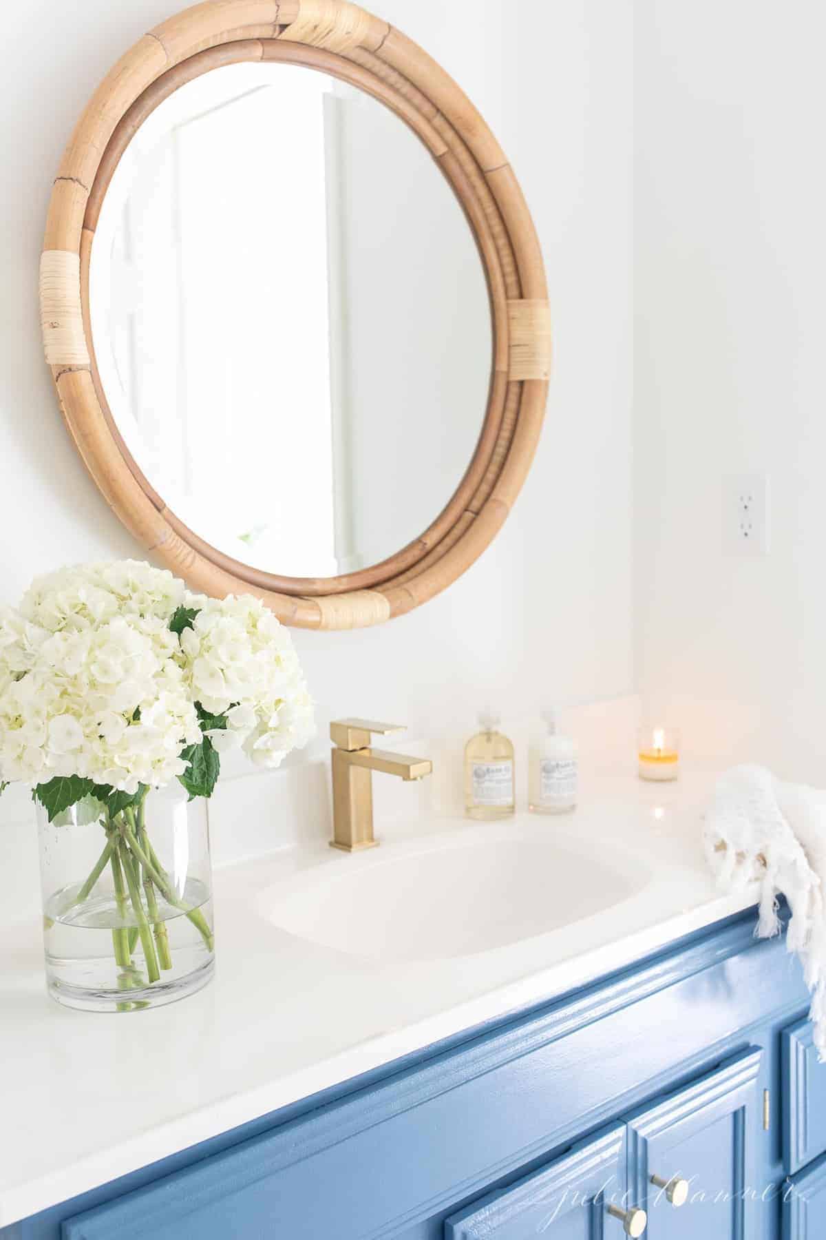 A nautical bathroom with a blue vanity and a round mirror.