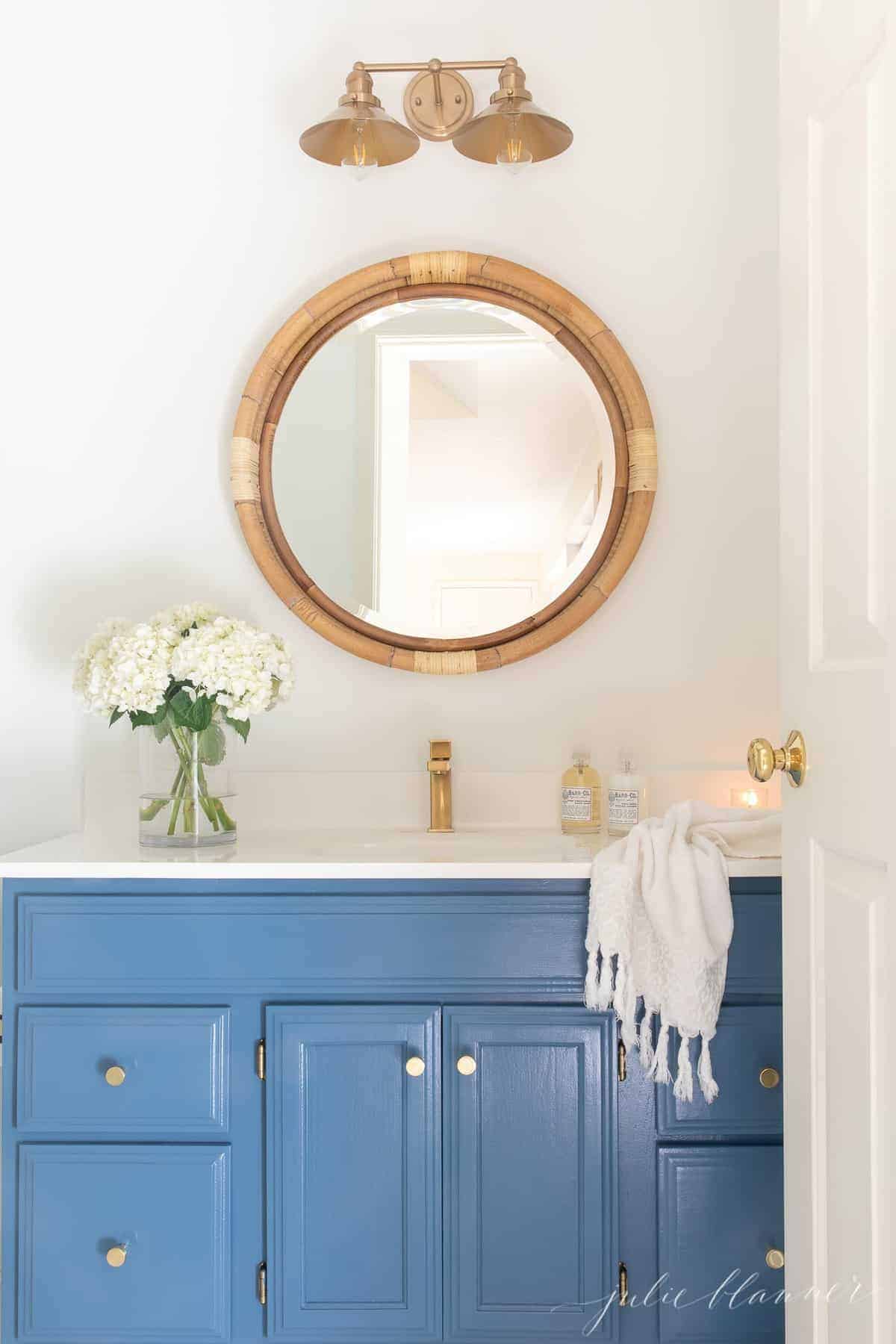 A nautical bathroom with a blue vanity and a round mirror.