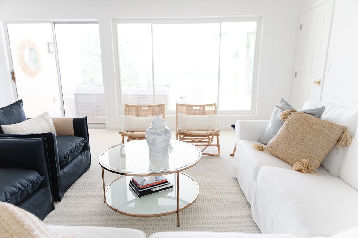 A white living room with a wall of windows, two navy blue chairs and a white sectional sofa.