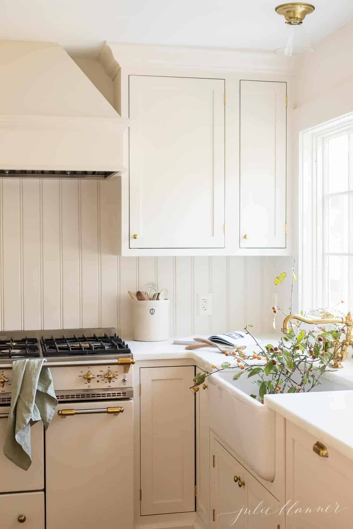 A white kitchen with shaker cabinet doors and marble counters, and fall branches in the sink.