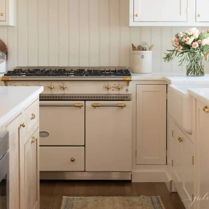 A white kitchen with shaker cabinets and marble counters, with a vase of flowers by the sink.