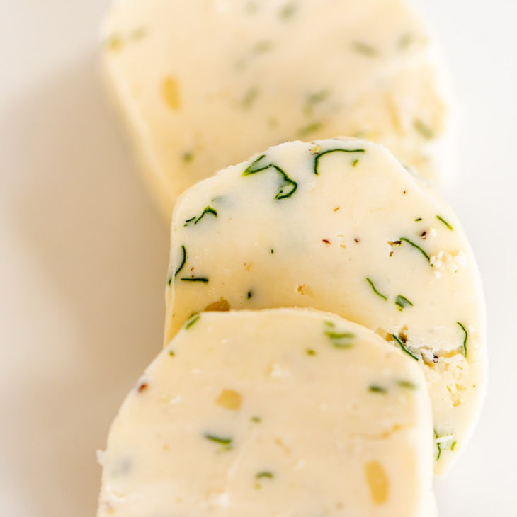 Three pats of herbed steak butter on a white surface.