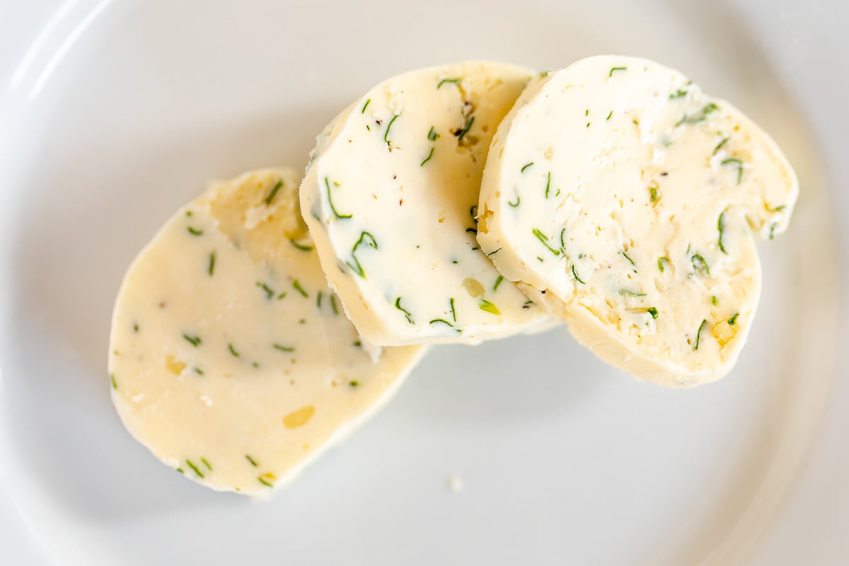 Three pats of herbed steak butter on a white surface.