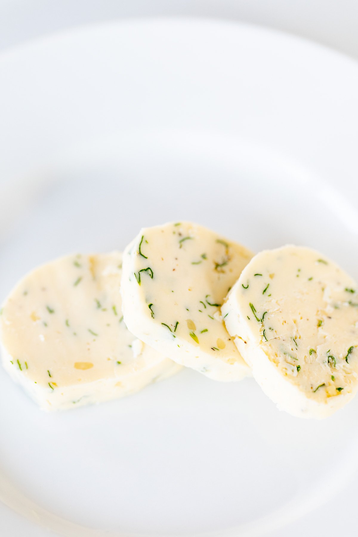 Three pats of herbed steak butter on a white surface.