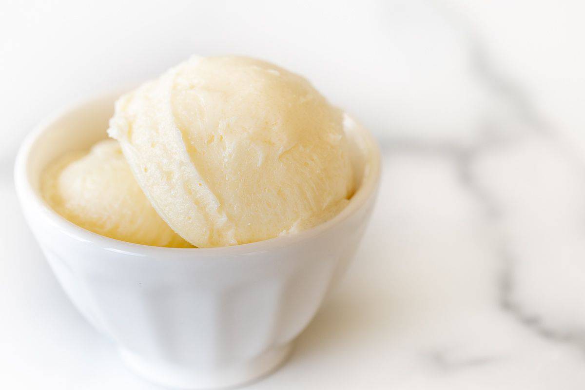 A small white bowl full of sweet butter on a marble counter top.