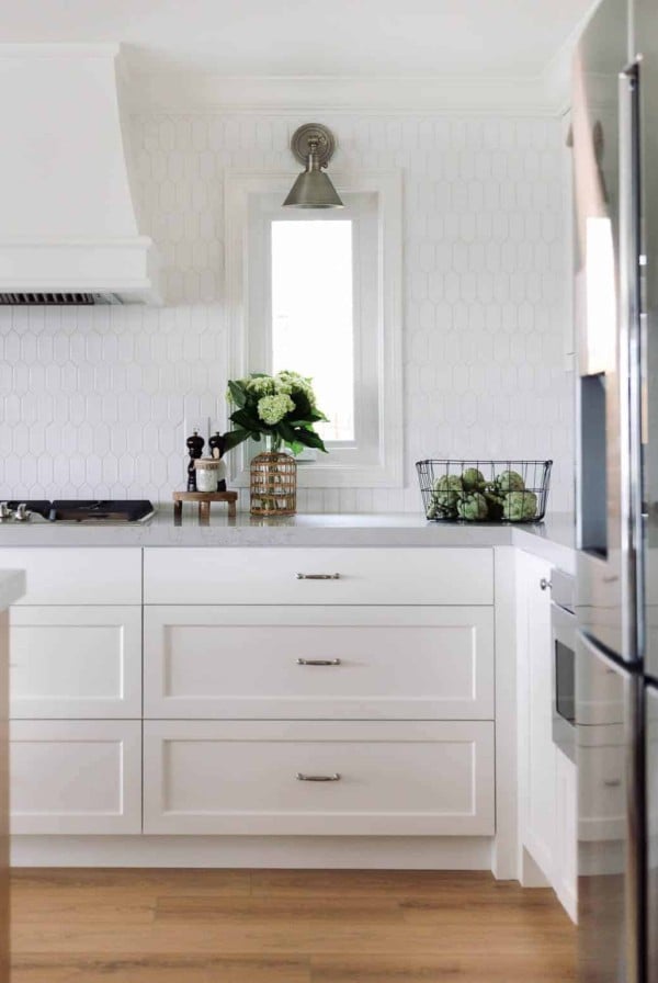 A kitchen with white hexagon tile backsplash and white cabinets.