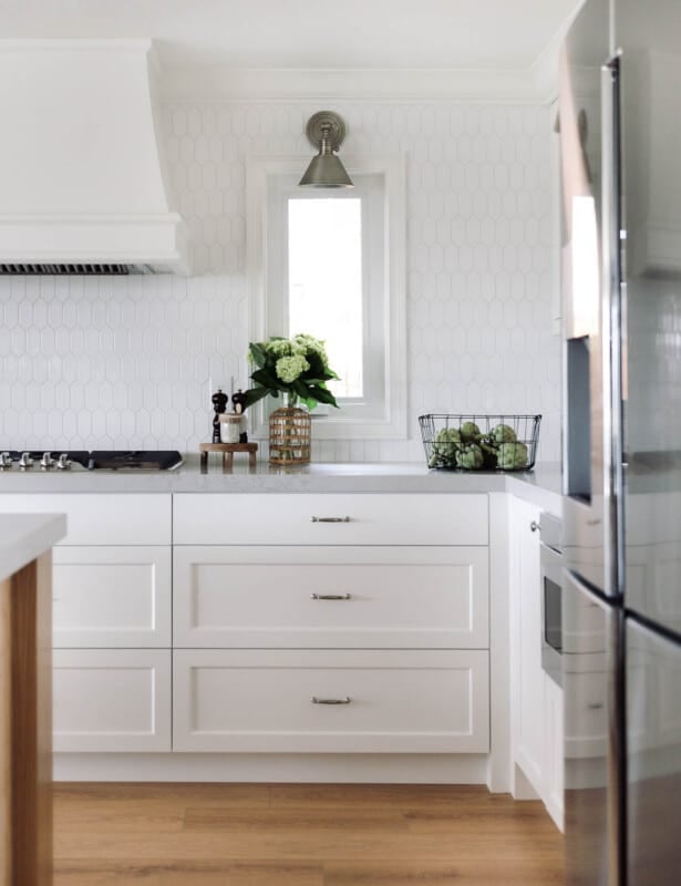 A kitchen with white hexagon tile backsplash and white cabinets.