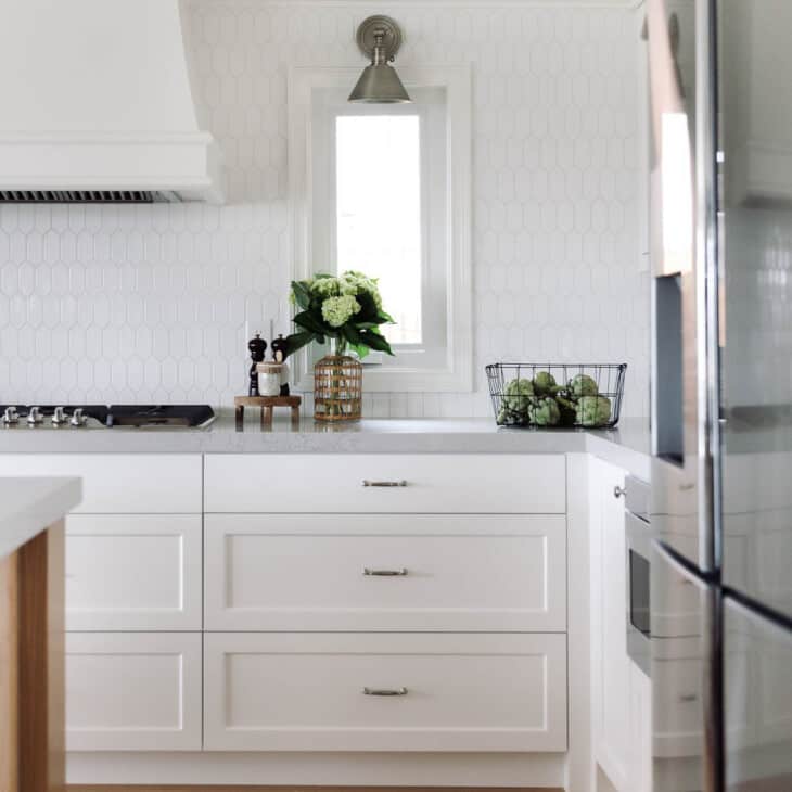 A kitchen with white hexagon tile backsplash and white cabinets.