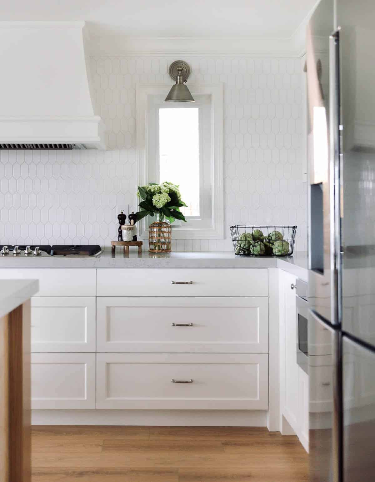 A kitchen with white hexagon tile backsplash and white cabinets.