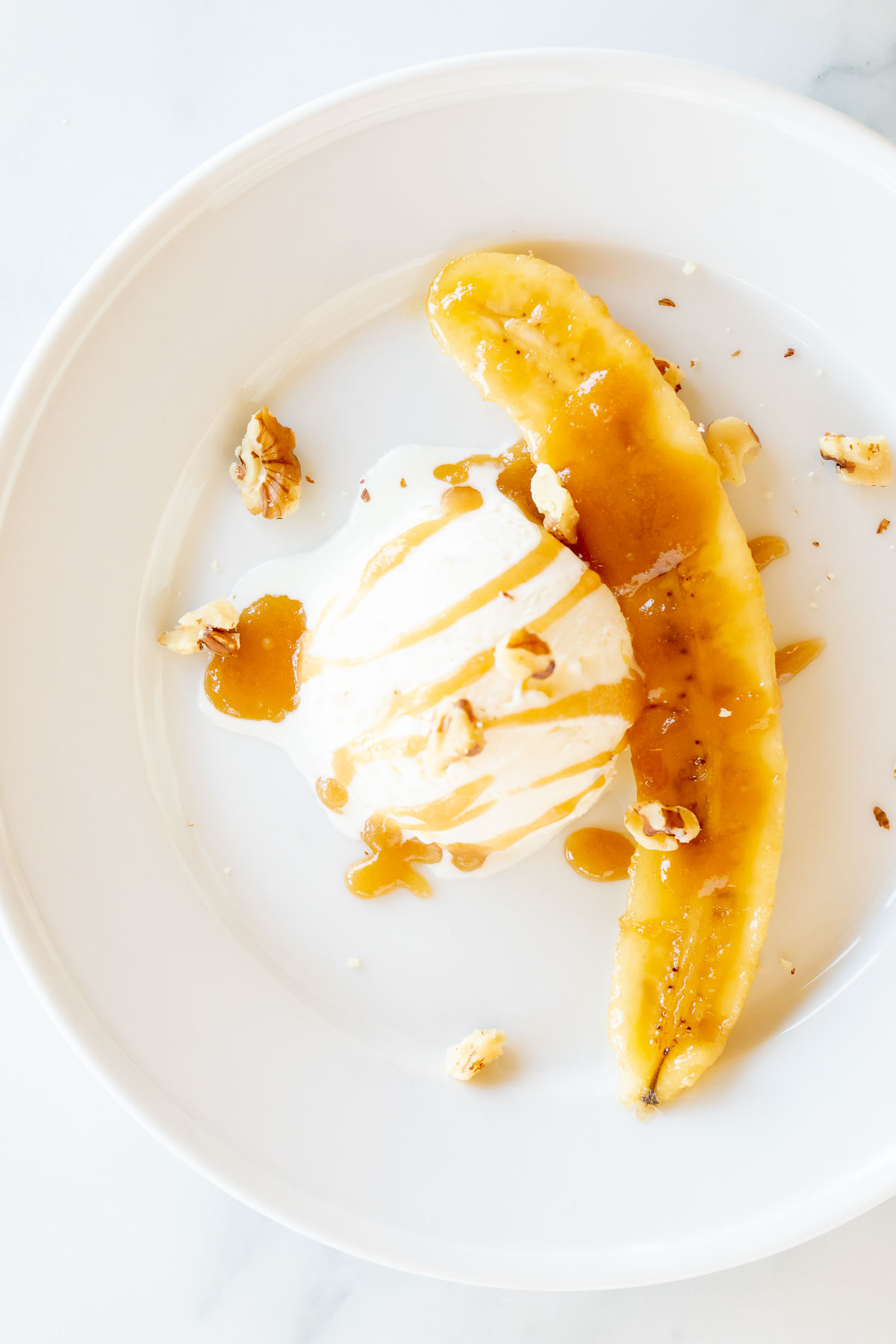 A white plate with a scoop of ice cream and a banana slice, perfect for making delicious Bananas Foster dessert.