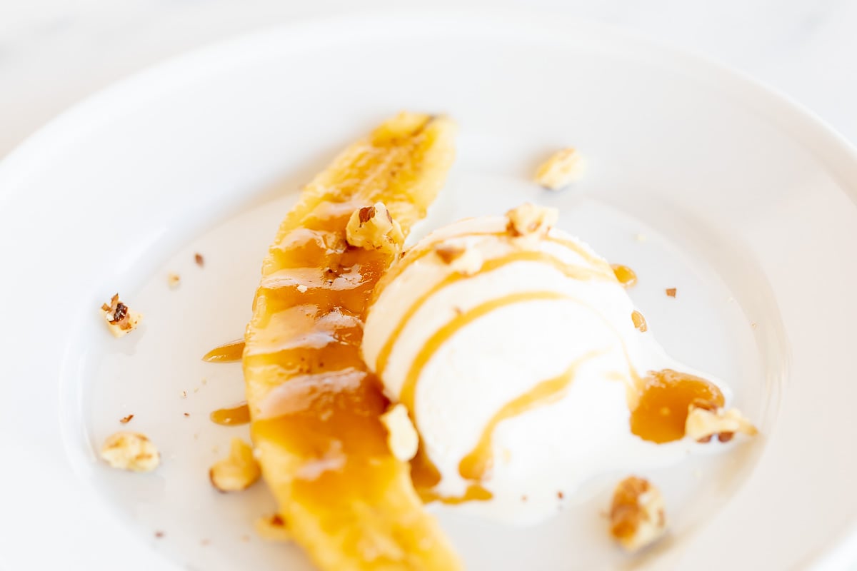 A plate with ice cream and a banana on it, topped with banana foster sauce.