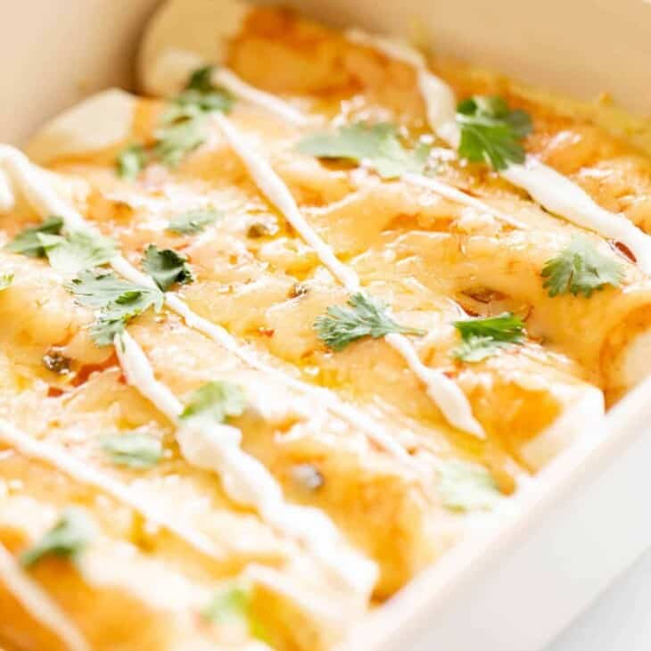 Close up view of these cheese enchiladas in a white baking dish.