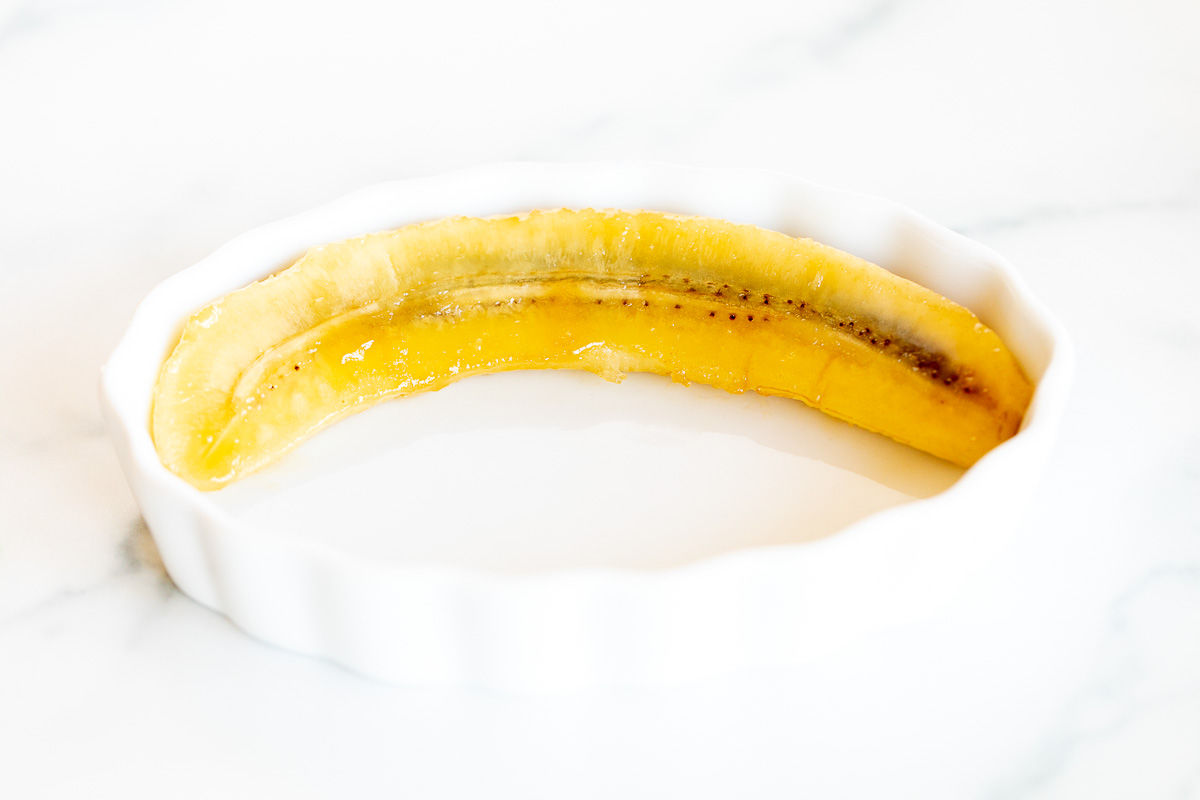 A slice of banana topped with a mouthwatering bananas foster sauce, elegantly presented in a white bowl.