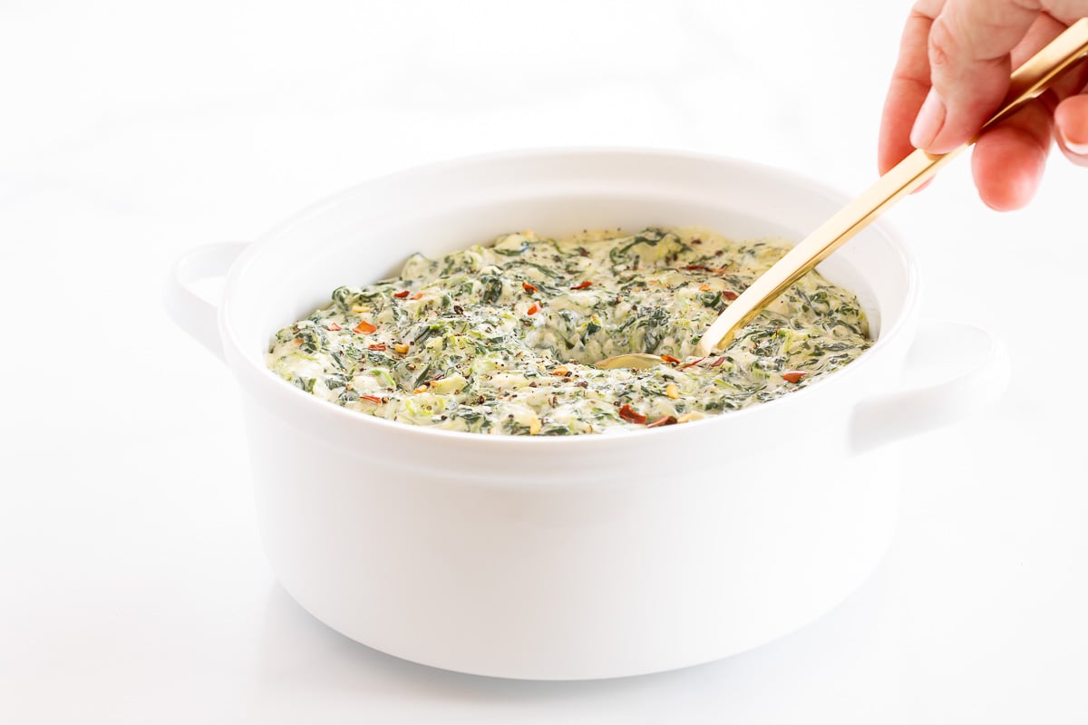 Cream cheese spinach dip in a white bowl with a gold spoon.