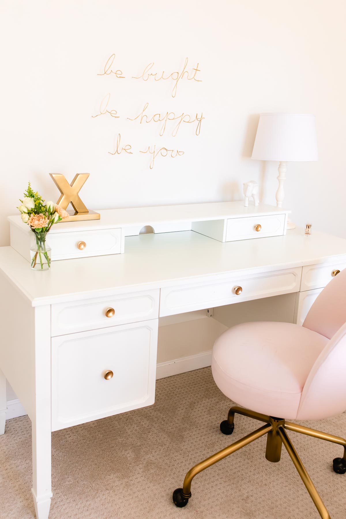 A white desk with a blush pink chair in a tween girl's bedroom