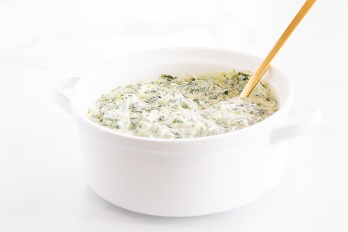 Cream cheese spinach dip in a white bowl with a wooden spoon.