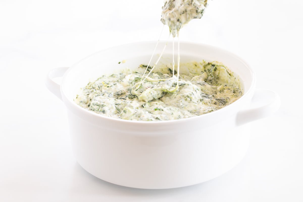 Cream cheese spinach dip being poured into a white bowl.