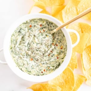 Spinach dip with cream cheese in a white bowl with chips.