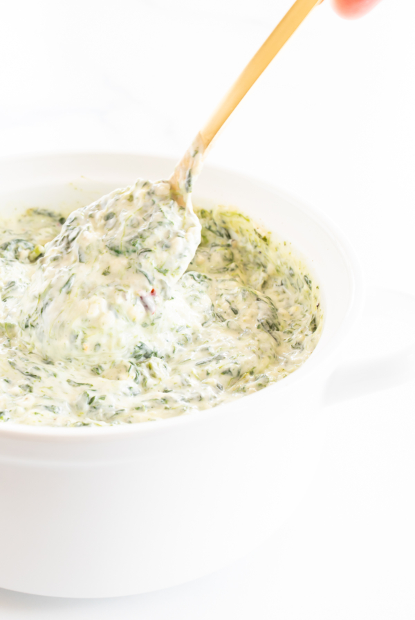 Spinach dip with cream cheese in a white bowl with a wooden spoon.