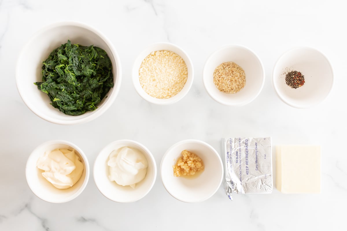 The ingredients for a spinach dip with cream cheese are laid out on a marble table.
