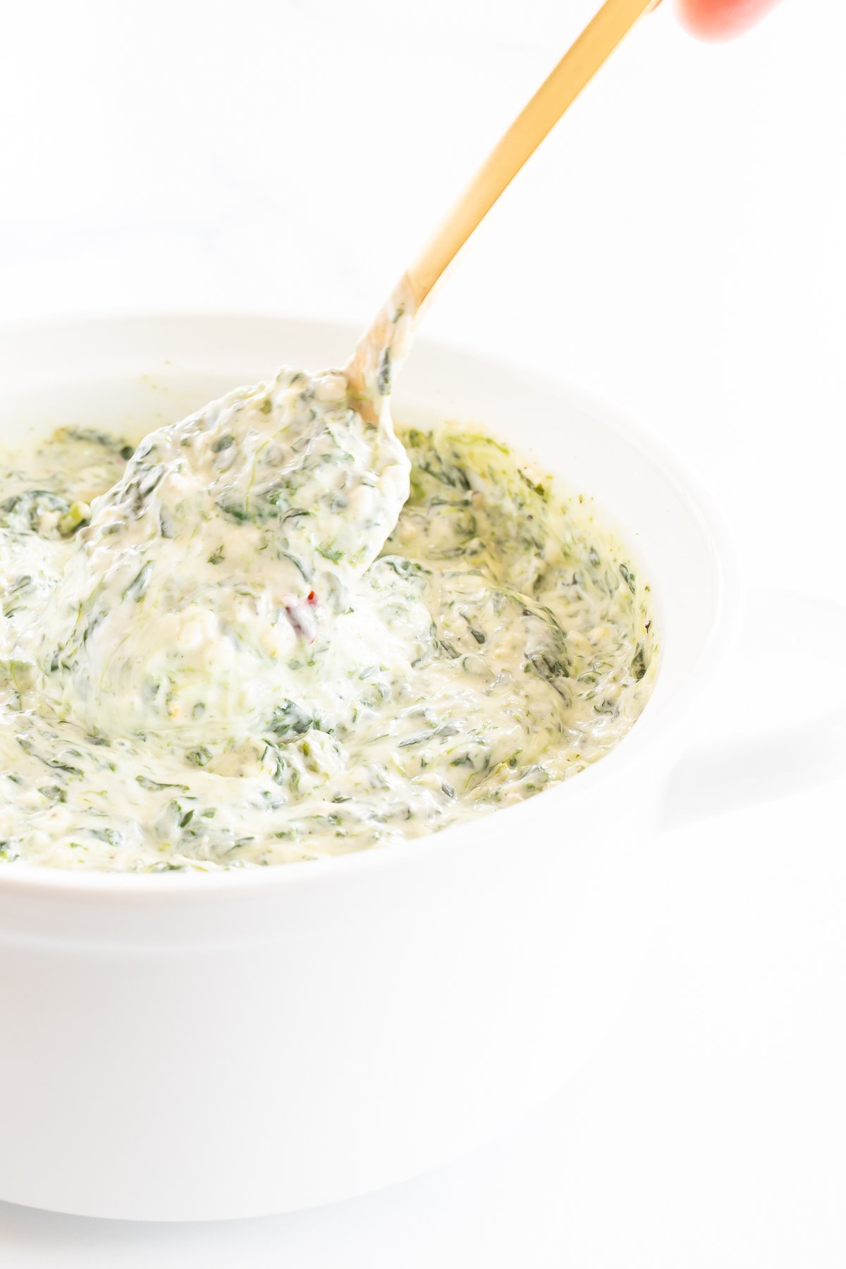Spinach dip with cream cheese in a white bowl with a wooden spoon.