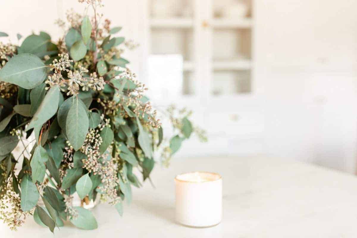 A vase of fresh eucalyptus on a marble island, white candle nearby.