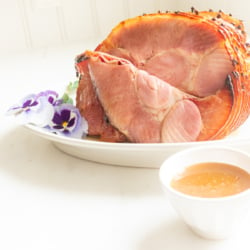 A sliced honey glazed ham on a white plate.