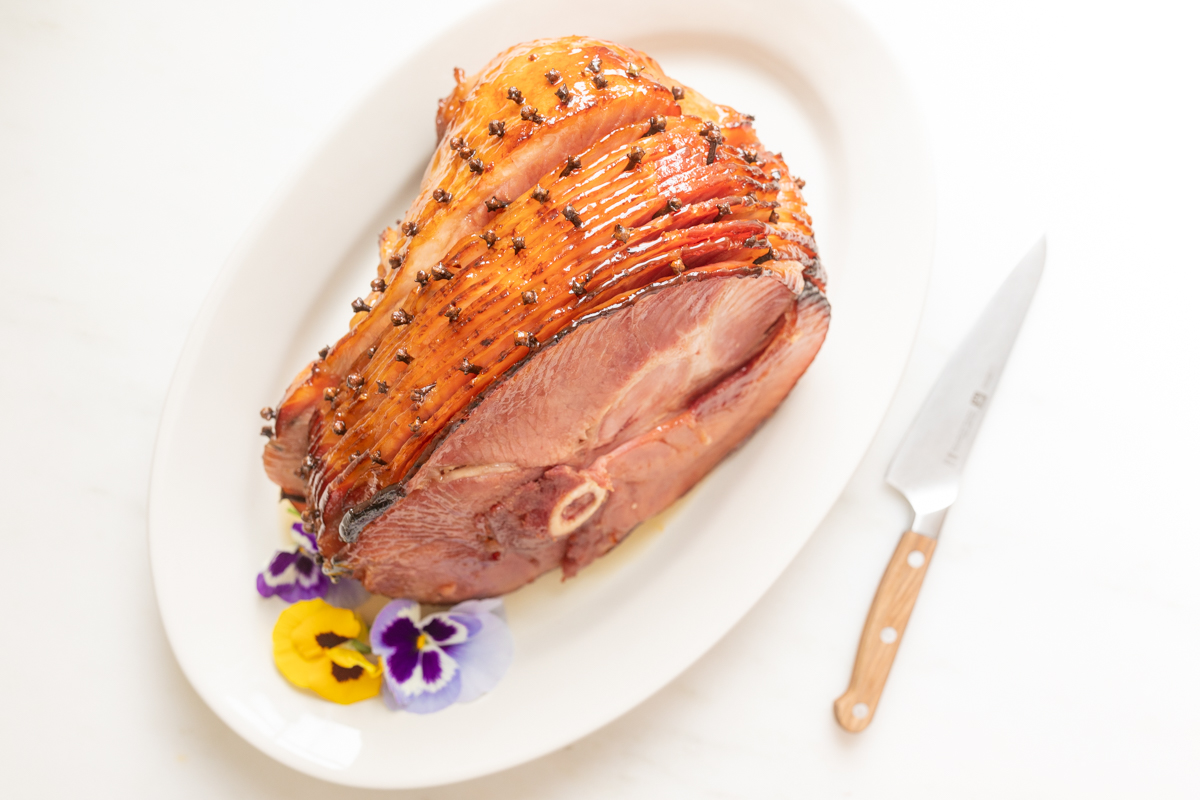 honey glazed ham garnished with fresh pansies on a white platter
