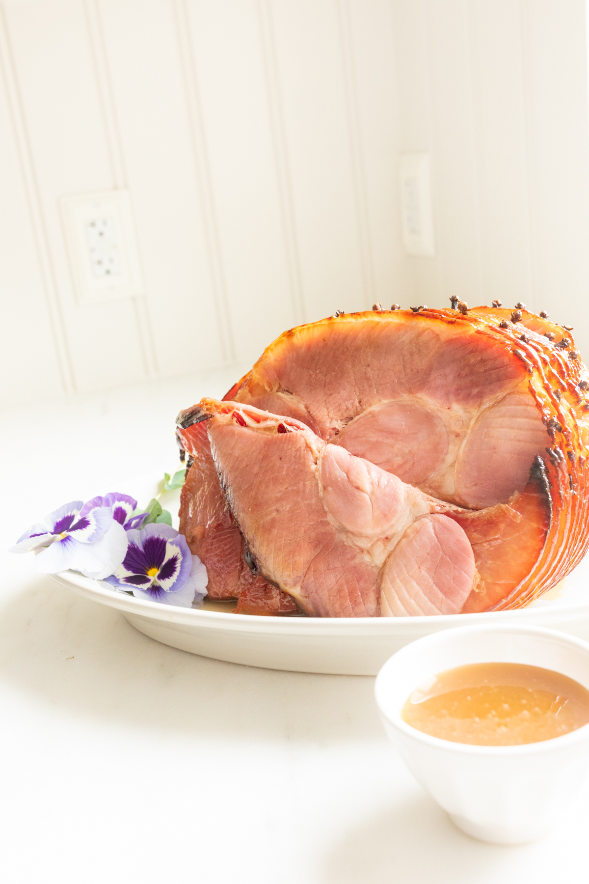honey glazed ham garnished with fresh pansies on a white platter