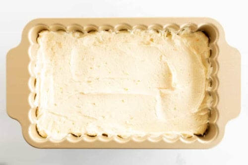 Orange pound cake batter in a rectangular baking dish on a white surface.