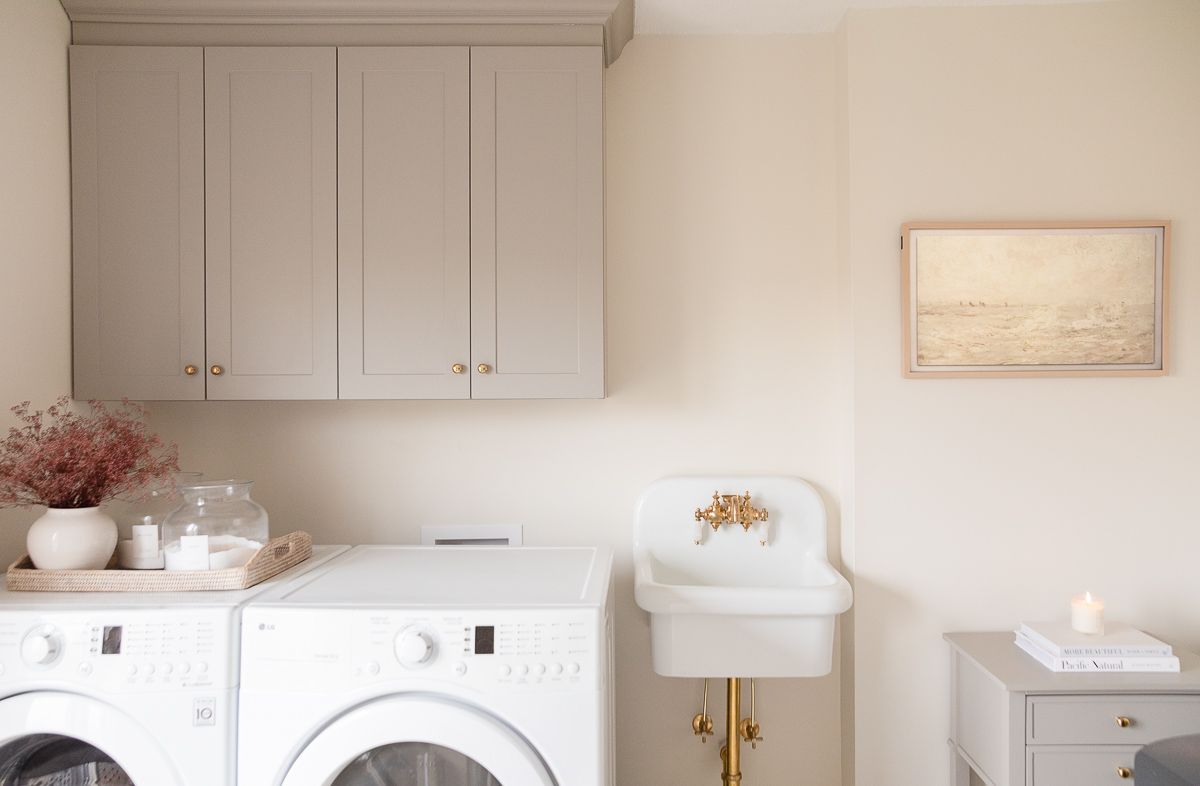 a laundry room with greige cabinetry and a wall sink